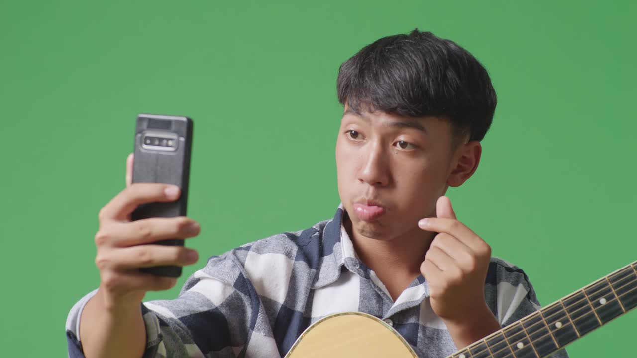 초록색 화면 배경에 서 있는 스마트폰에서 기타 셀피를 찍은 아시아 십대