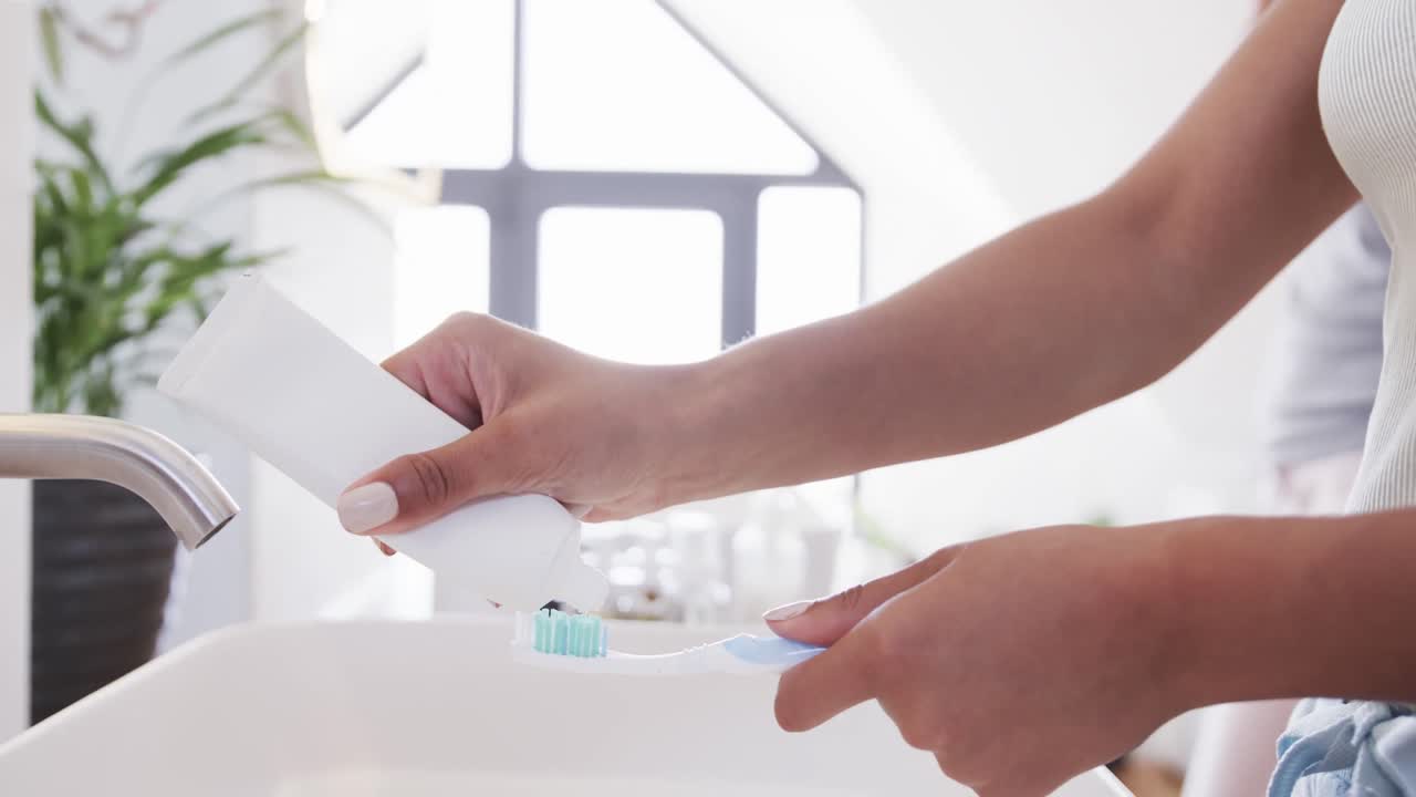 Midsection of biracial lesbian couple brushing teeth in the morning in sunny bathroom, slow motion