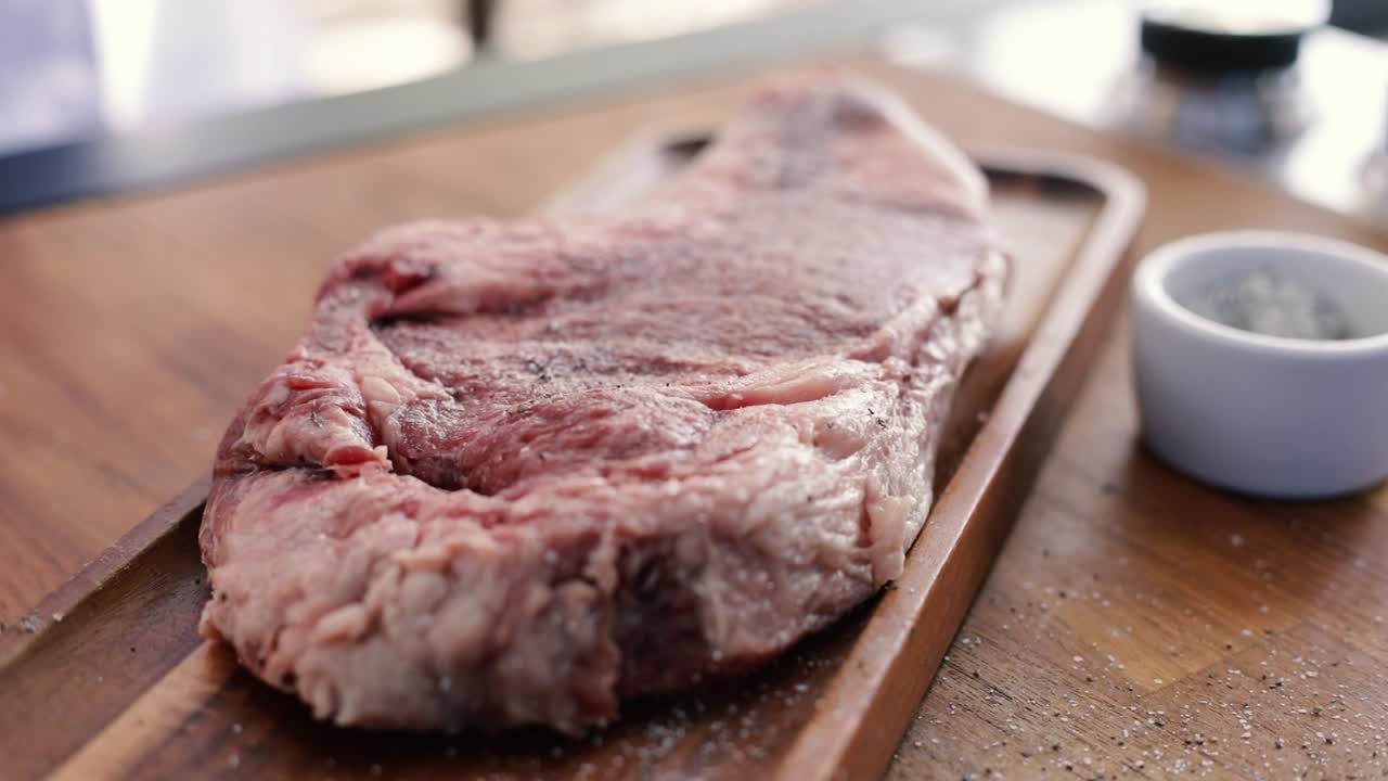 Person seasoning steak with salt and pepper closeup