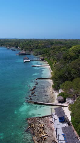 vertical drone shot of beachfront of green tropical island, waterfront homes and docks