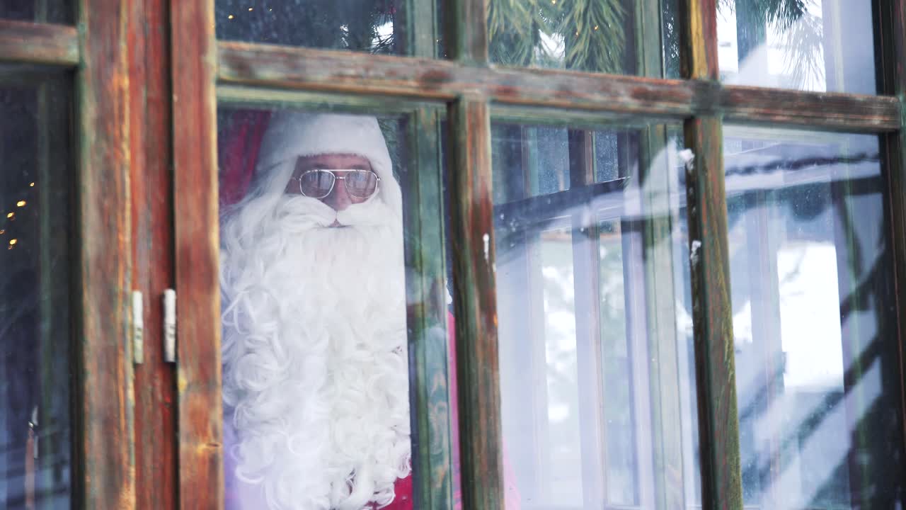 Santa Claus looking through the window. View from outdoors into the house with Santa in glasses. Xmas time