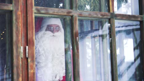 santa claus looking through the window. view from outdoors into the house with santa in glasses. xmas time