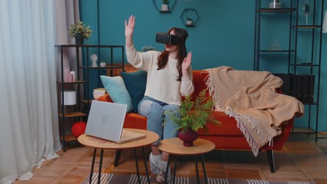 una mujer joven usa gafas de realidad virtual en casa, disfrutando del concepto de video moviendo las manos en el aire