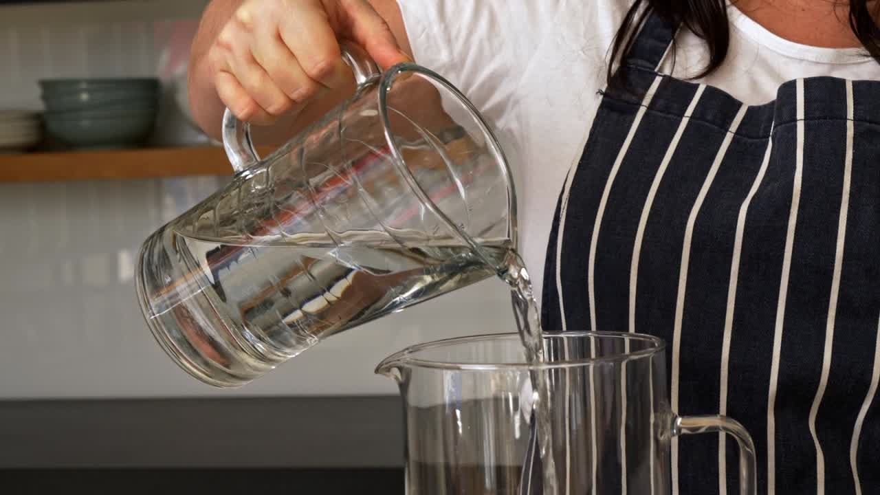 Female chef pours water from glass container into another glass pitcher