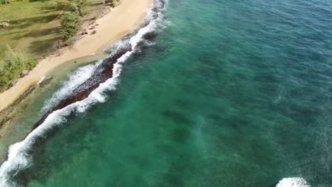 Turquoise-ocean-water-foaming-at-the-shore,-washing-the-golden-sand-of-the-beach-with-footprints,-Idyllic-summer-vacation-in-Hawaii