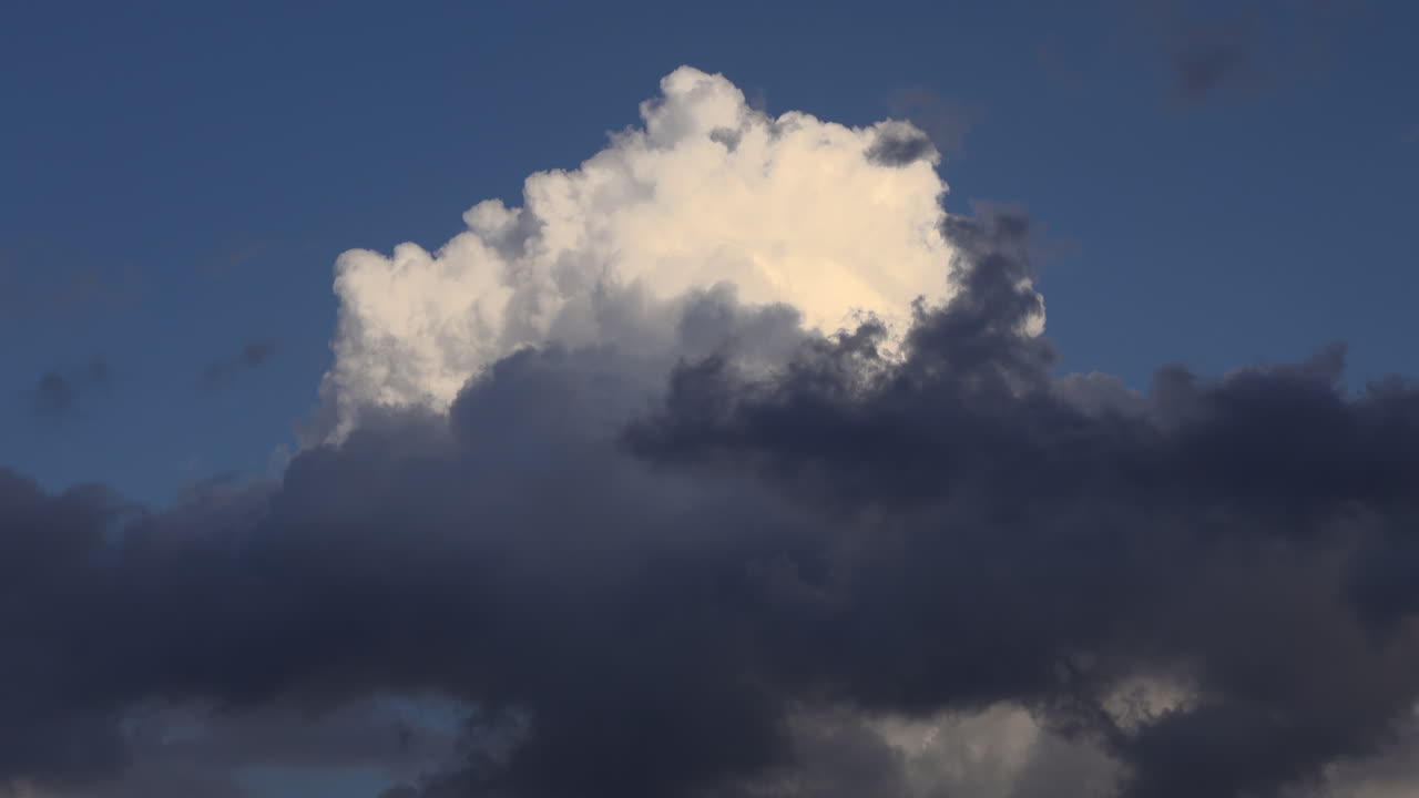 Sunlit white cloud rising above a layer of darker clouds against a deep blue sky