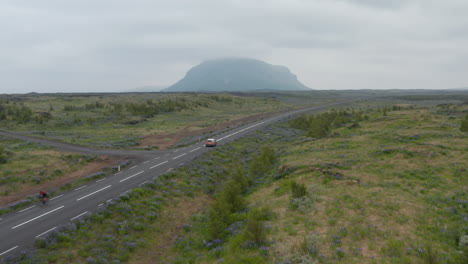 Birds-eye-view-car-peacefully-driving-on-ring-road,-the-most-important-highway-in-Iceland.-Aerial-view-of-car-driving-down-straight-road-through-grassy-highlands-valley