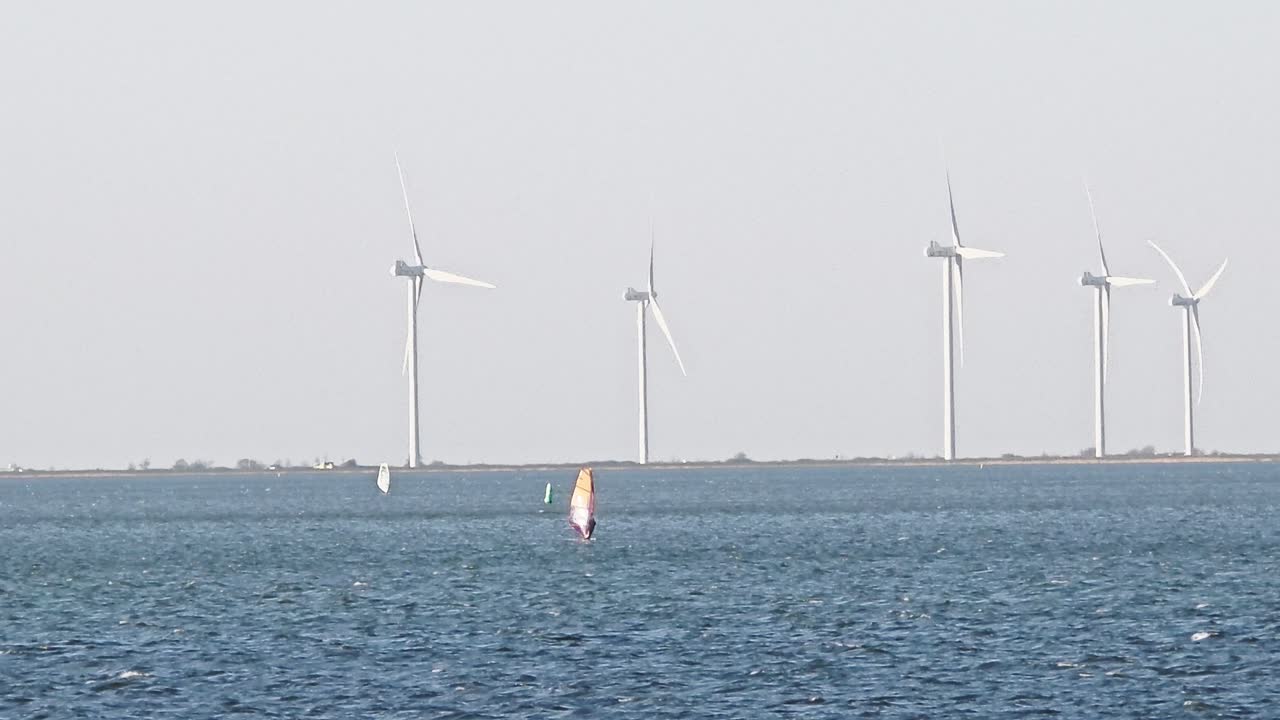 Wind surfers on a sunny day with wind turbines in the background