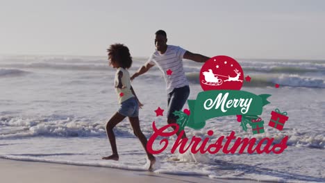 animation of merry christmas over happy afrian american father and daughter having fun on beach