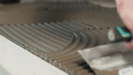 close up of a worker spreading tile adhesive with a notched trowel