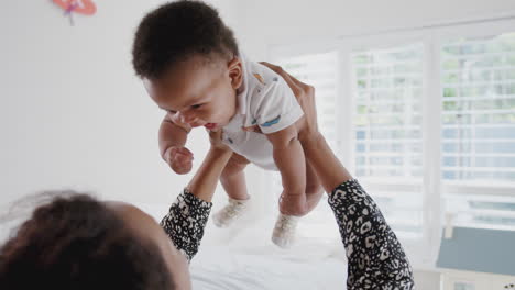 Mother-Cuddling-And-Playing-With-Baby-Son-In-Nursery-At-Home-Lifting-Him-In-Air