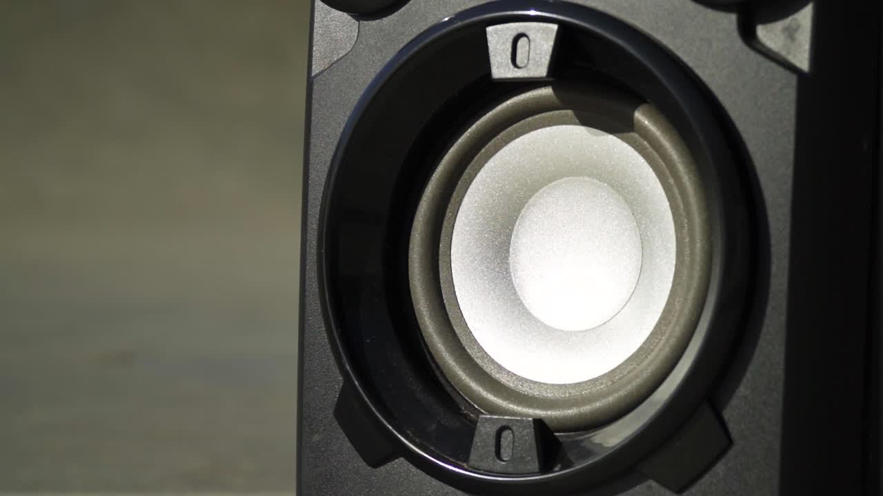 close up zooming in on a speaker blasting out music bass creating shake of the disk inside the plastic speaker bouncing moving with the flow of the song silver inside placed outdoor listening closely