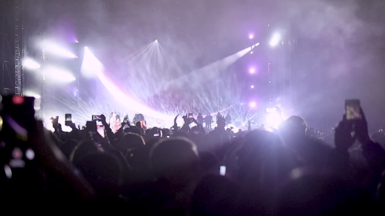 Large crowd of fans in front of a stage dancing with lightshow