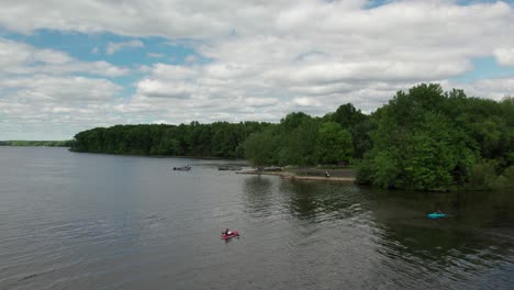 aerial drone shot of tourists kayaking over a lake beside a park on a cloudy day