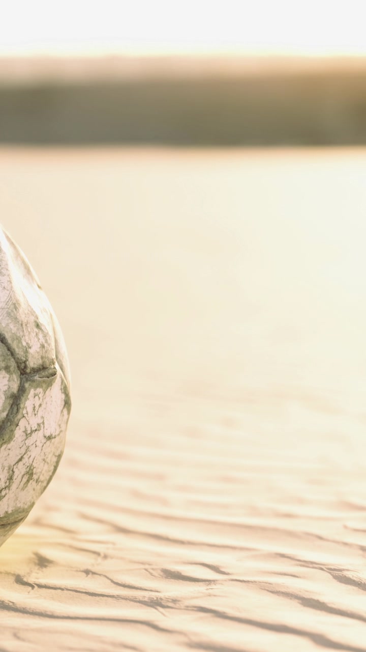 Vecchio pallone da calcio su una spiaggia sabbiosa al tramonto vicino all'acqua