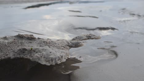 low angle view of water flowing across a sandy beach erodes the sand and melting ice forming beautiful organic shapes. water reflections on wet sand and melting frost while while water gently flows
