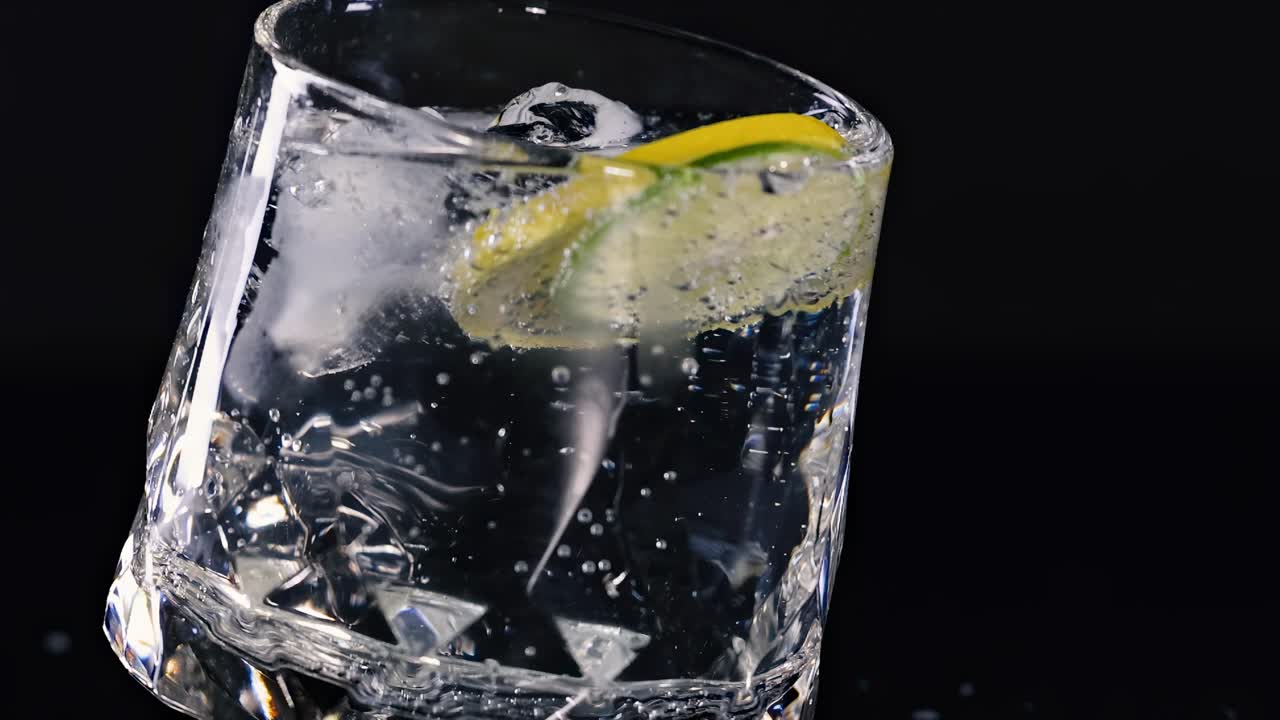 Un primo piano di un bicchiere inclinato con una fetta di lime e bollicine effervescenti su uno sfondo scuro.