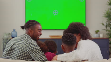 rear view of family sitting on sofa at home watching green screen tv and laughing at comedy - shot in slow motion