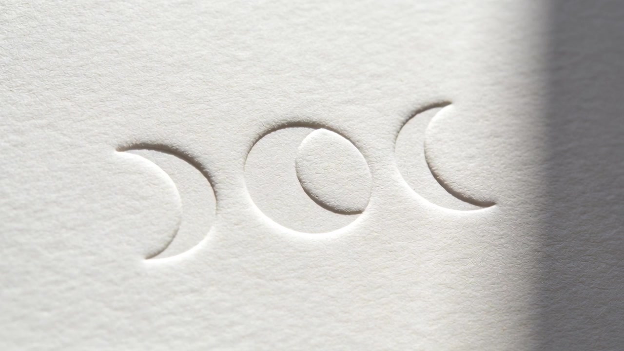 Una stretta banda d'ombra si sposta, attraversando tre mezzelune in rilievo in primo piano, rivelando la texture della carta.