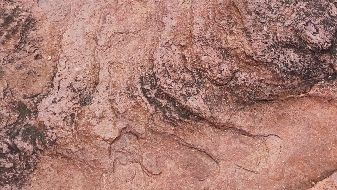 Ripresa in movimento su arenaria erosa che rivela intricate texture sedimentarie, macchie minerali e formazioni geologiche naturalmente scolpite