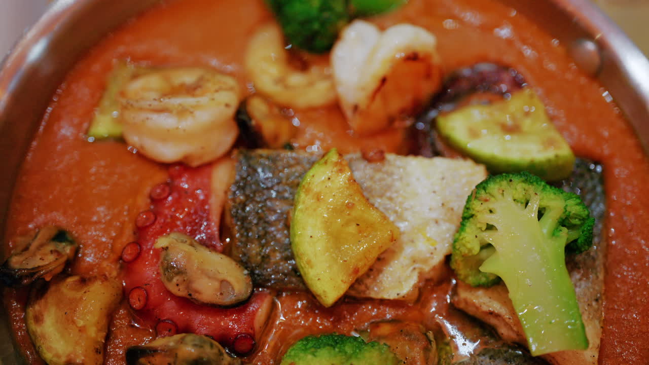 Primo piano di un piatto gourmet di frutti di mare in una salsa ricca con pesce, polpo, crostacei e verdure.