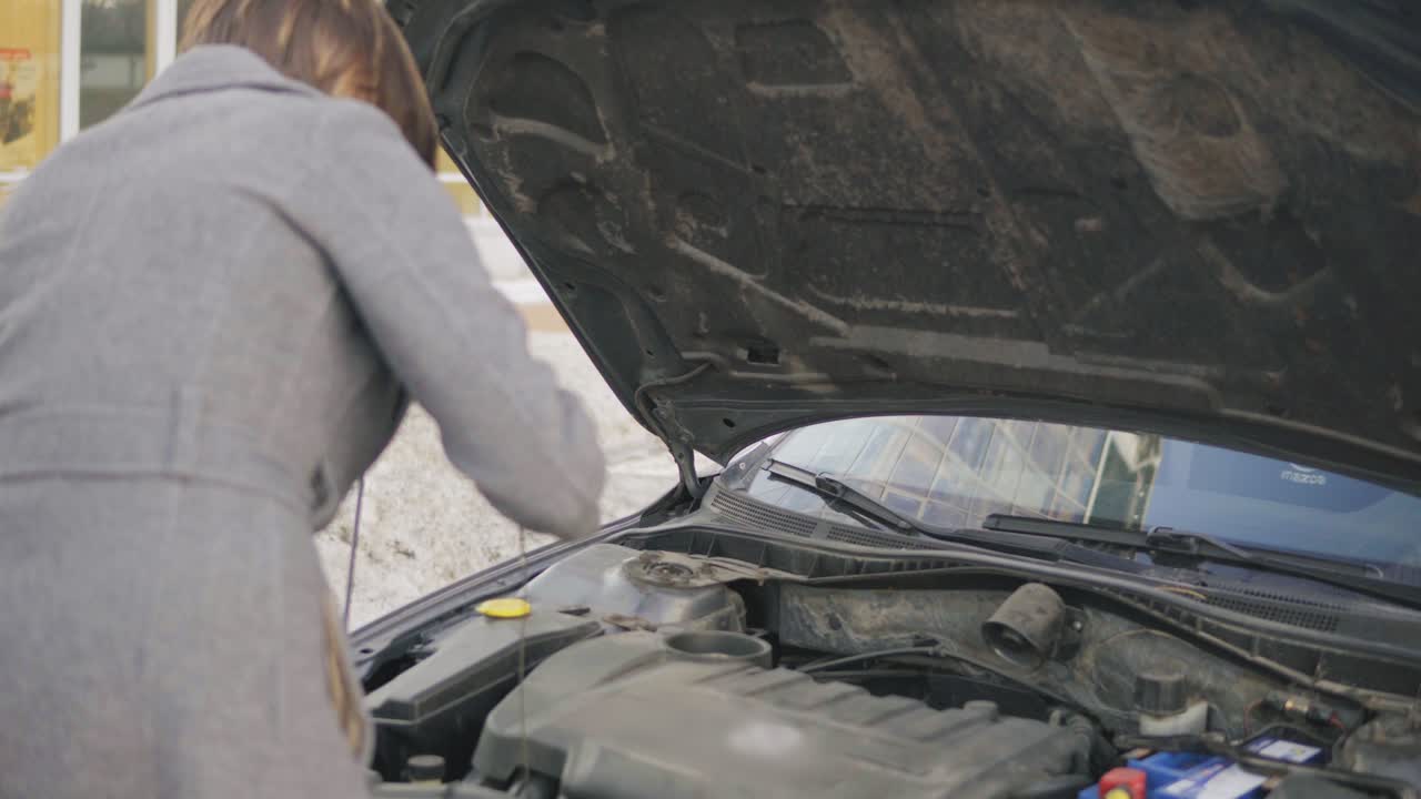 Business woman checks the oil level in the car looking under the hood in the street