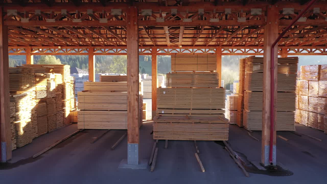A smooth tracking shot moves through a lumber warehouse. Neatly organized stacks of finished wood planks and boards are ready for shipping, representing inventory and logistics