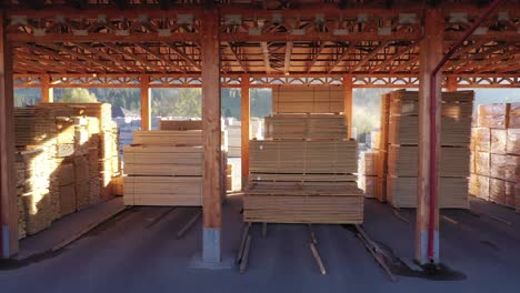 A smooth tracking shot moves through a lumber warehouse. Neatly organized stacks of finished wood planks and boards are ready for shipping, representing inventory and logistics