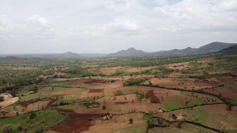 High-altitude-Drone-shot-over-a-tribal-savanna-area-with-straw-hut-houses-and-farmland-in-Omo-Valley-with-mountains-in-the-background