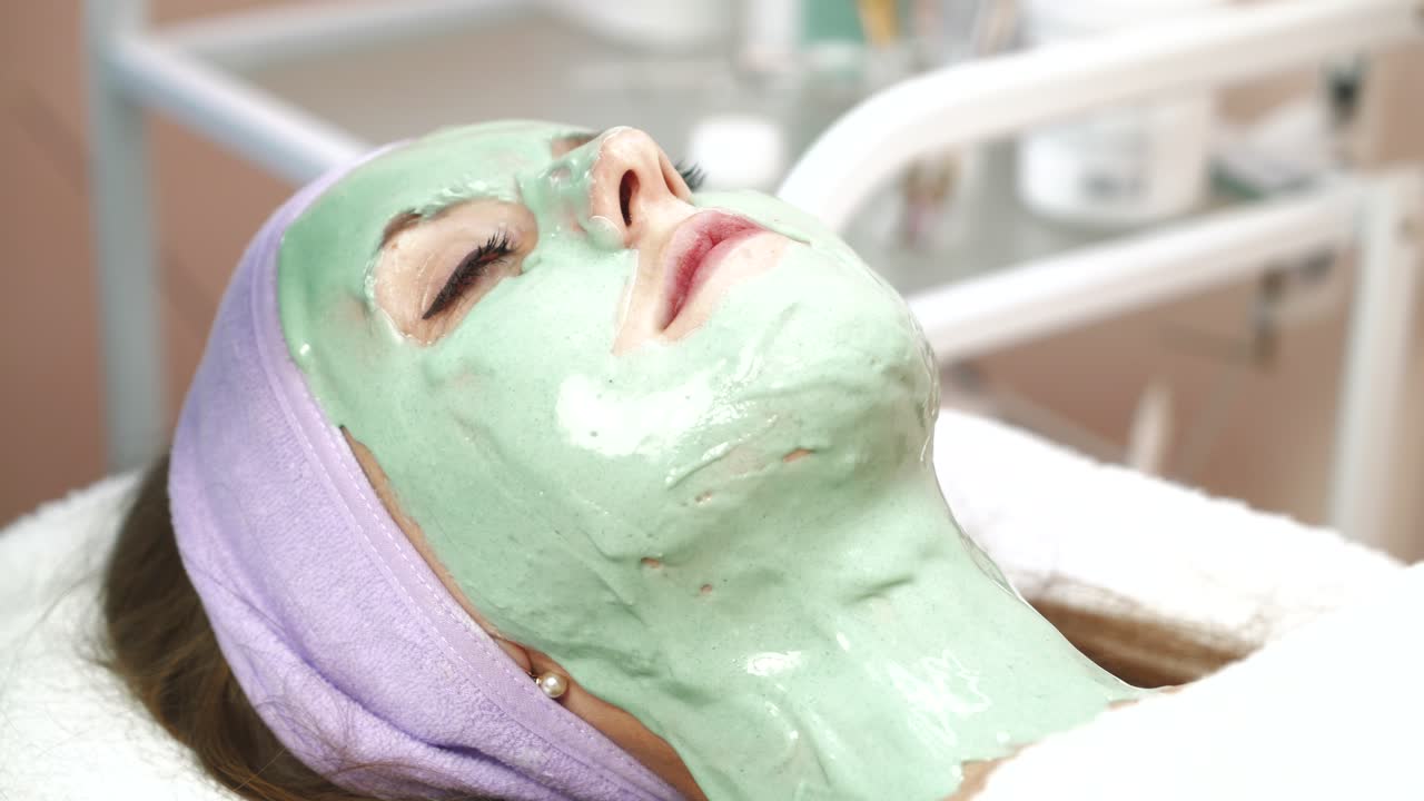 Facial dry skin and body care. Cosmetologist smears cosmetic mask on the face of woman