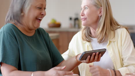 laughing , multiracial senior female friends watching video on smartphone, enjoying time, at home