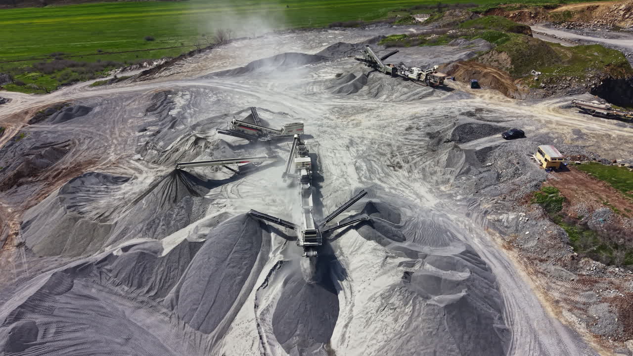 Granite quarry with processing equipment and stockpiles in daylight showing active mining operations in a rural area