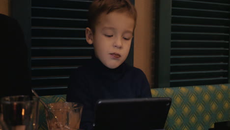 un niño en un café comiendo helado y viendo una tableta digital.