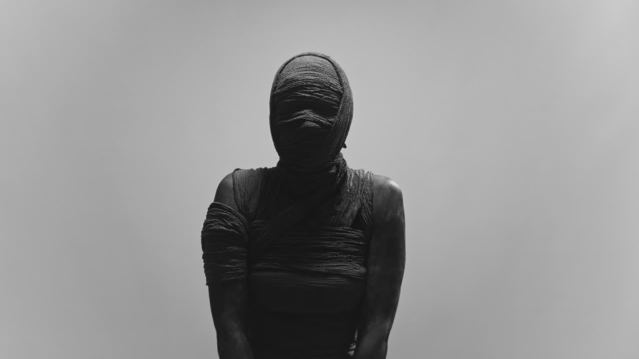 A mummy of a woman on a white backdrop slowly rises her head