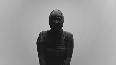 a mummy of a woman on a white backdrop slowly rises her head