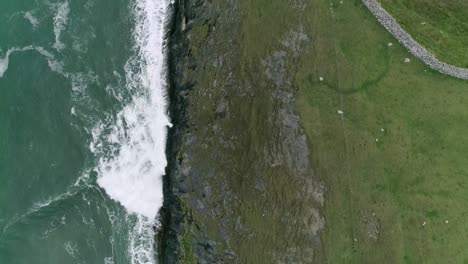 Abstrakte,-Halb-Und-Halb-Von-Oben-Nach-Unten-Gerichtete-Luftaufnahmen-Von-Grünen-Felsigen-Küstenklippen-Und-Rauen-Türkisfarbenen-Meereswellen,-Die-Am-Rande-Der-Landzunge-Entlanglaufen