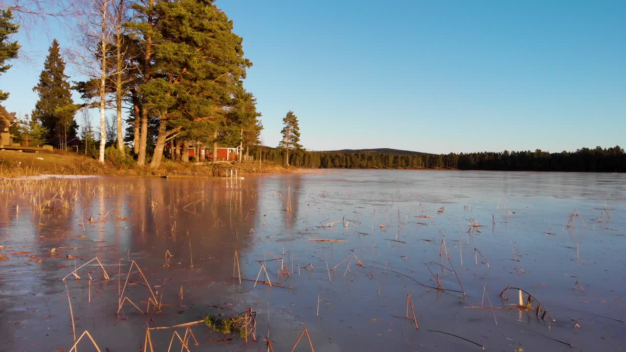 avanzando cerca del hielo sobre el lago busjon con una cabaña roja entre los pinos en un soleado día de invierno en applebo, vansbro kommun