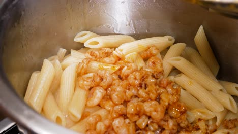 pouring freshly cooked small shrimps on steaming hot boiled pasta