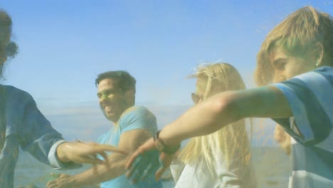 multi-ethnic group of young people throw colorful powder at each other in celebration of holi festival. they have enormous fun on this clear day by the sea.