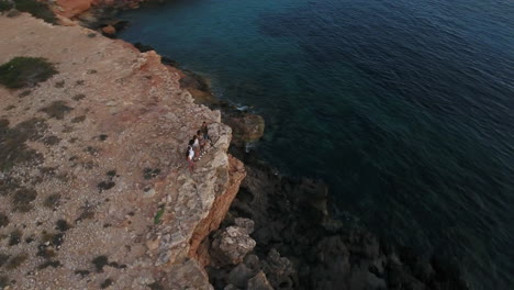 aerial shot of friends on cliffs watching sun set over sea