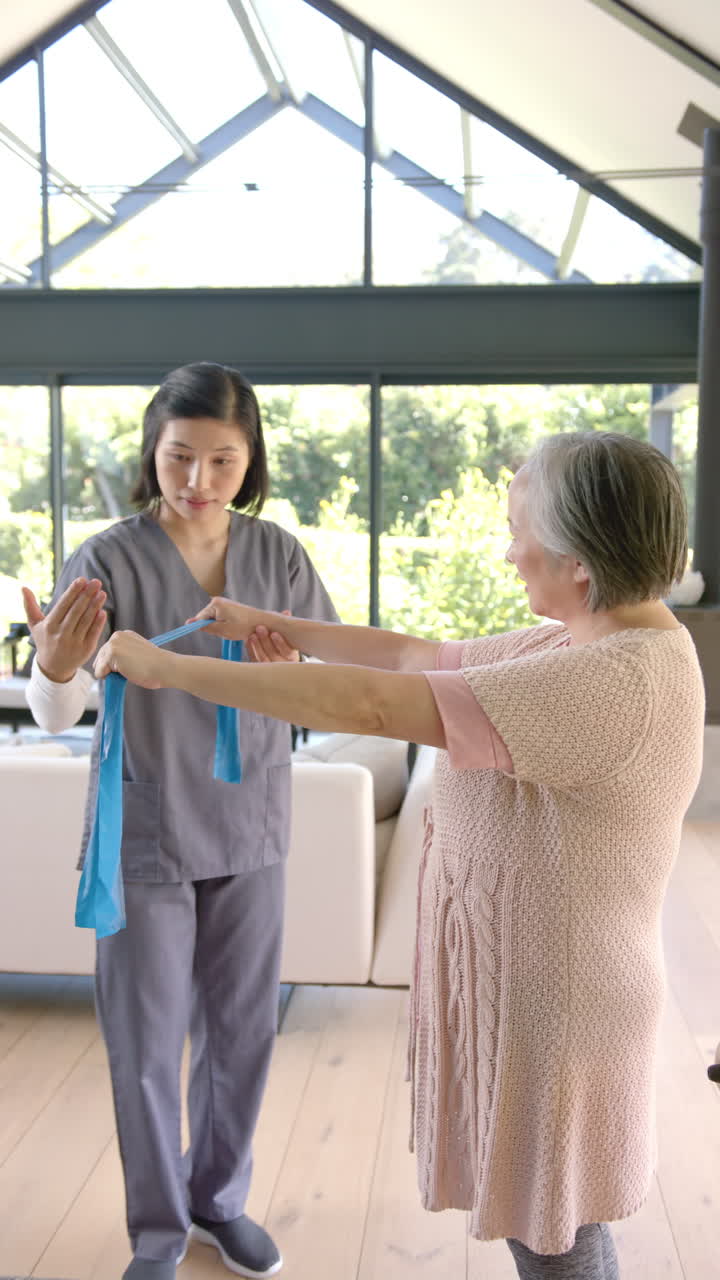 Vertical video: Physical therapist assisting senior woman with resistance band exercises at home