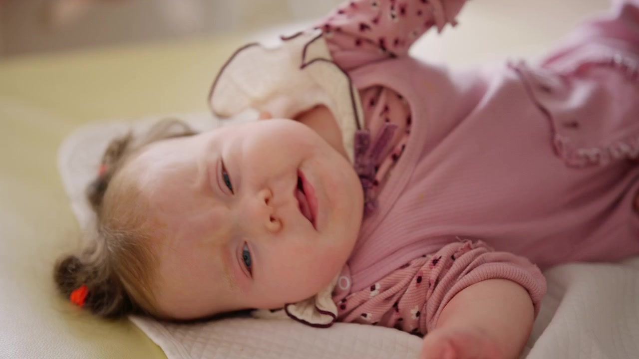 En baby ligger på et mykt stelleunderlag mens en voksen forsiktig beveger armene hennes