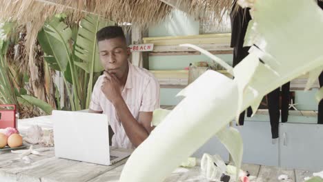 Fröhlicher-Afroamerikanischer-Mann-Mit-Laptop-Hinter-Der-Theke-Der-Surf-Verleih-Strandhütte,-Zeitlupe