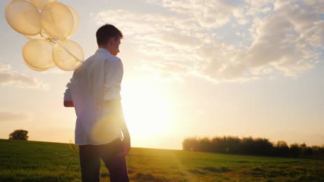 a teenager in a white smart shirt with balloons in his hand. goes in a picturesque place towards the sunset