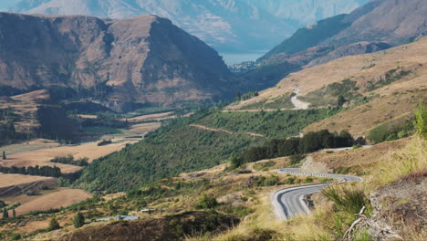 un camino de montaña empinado y sinuoso se abre camino hacia la vibrante ciudad de queenstown, nueva zelanda.