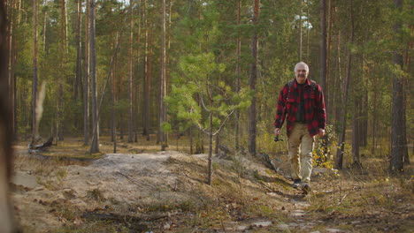 fisherman-with-rod-in-hand-is-walking-on-shore-between-high-pines-at-autumn-day-hiking-and-camping-at-vacation-and-holidays