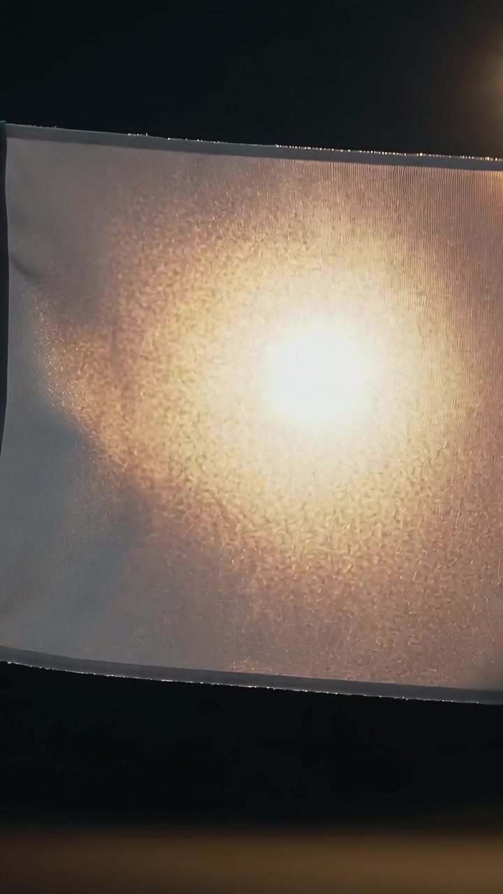 Video verticale: Lampada che si accende, pannello di tessuto che ondeggia in studio, rivelando pieghe calde retroilluminate