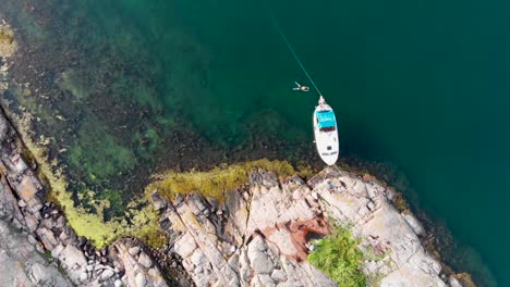 Vuelo-Aéreo-Descendente-De-Drones-Hacia-Un-Pequeño-Bote-Atracado-En-La-Costa-Rocosa-De-Bohuslan,-Suecia