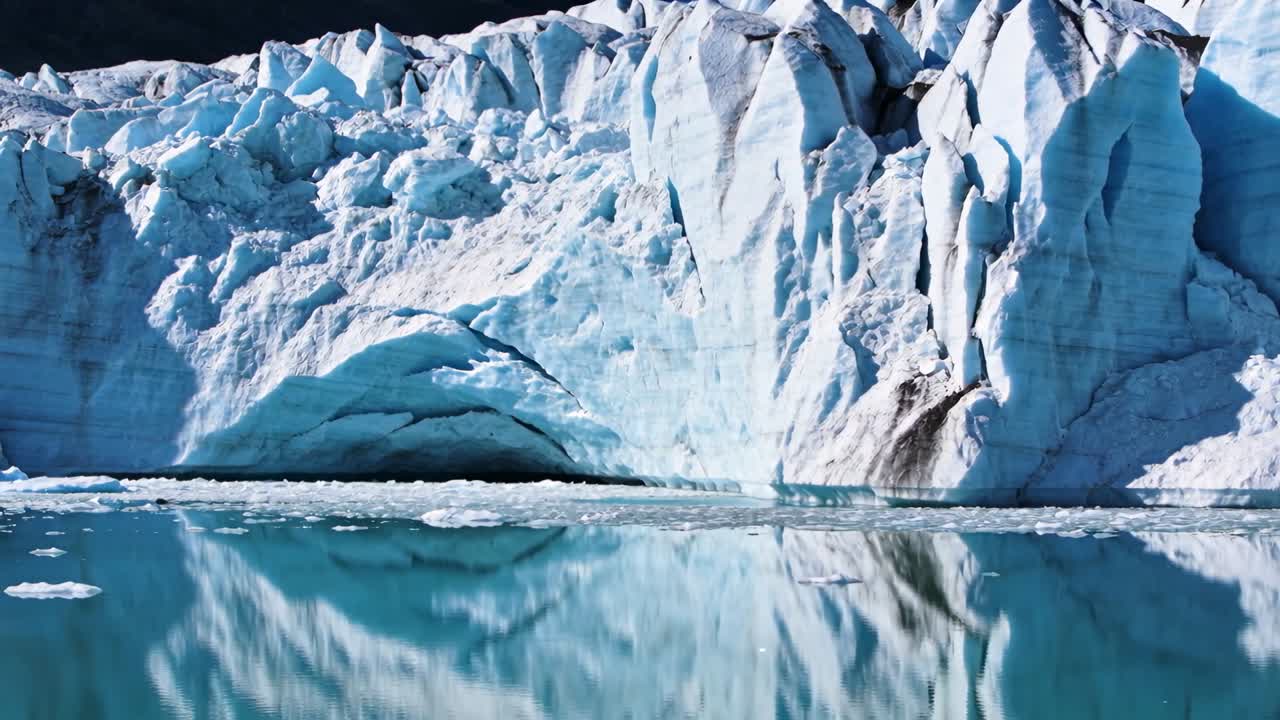 Fronte di ghiacciaio che si stacca rilasciando blocchi di ghiaccio in acqua turchese, rivelando crepacci e increspature.