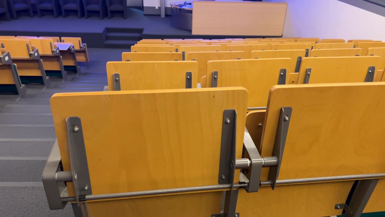 A wide shot of an empty academic auditorium with tiered wooden desks and chairs, suitable for educational or corporate presentation themes.